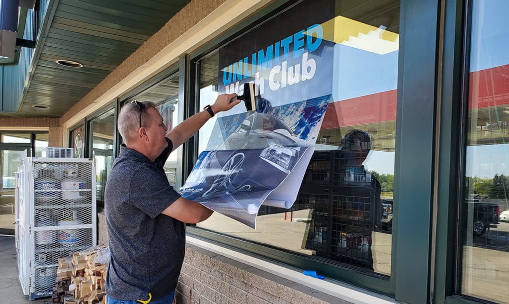 A Rogue Signs employee installs a vinyl window wrap outside of Dusterhoft Family Stores