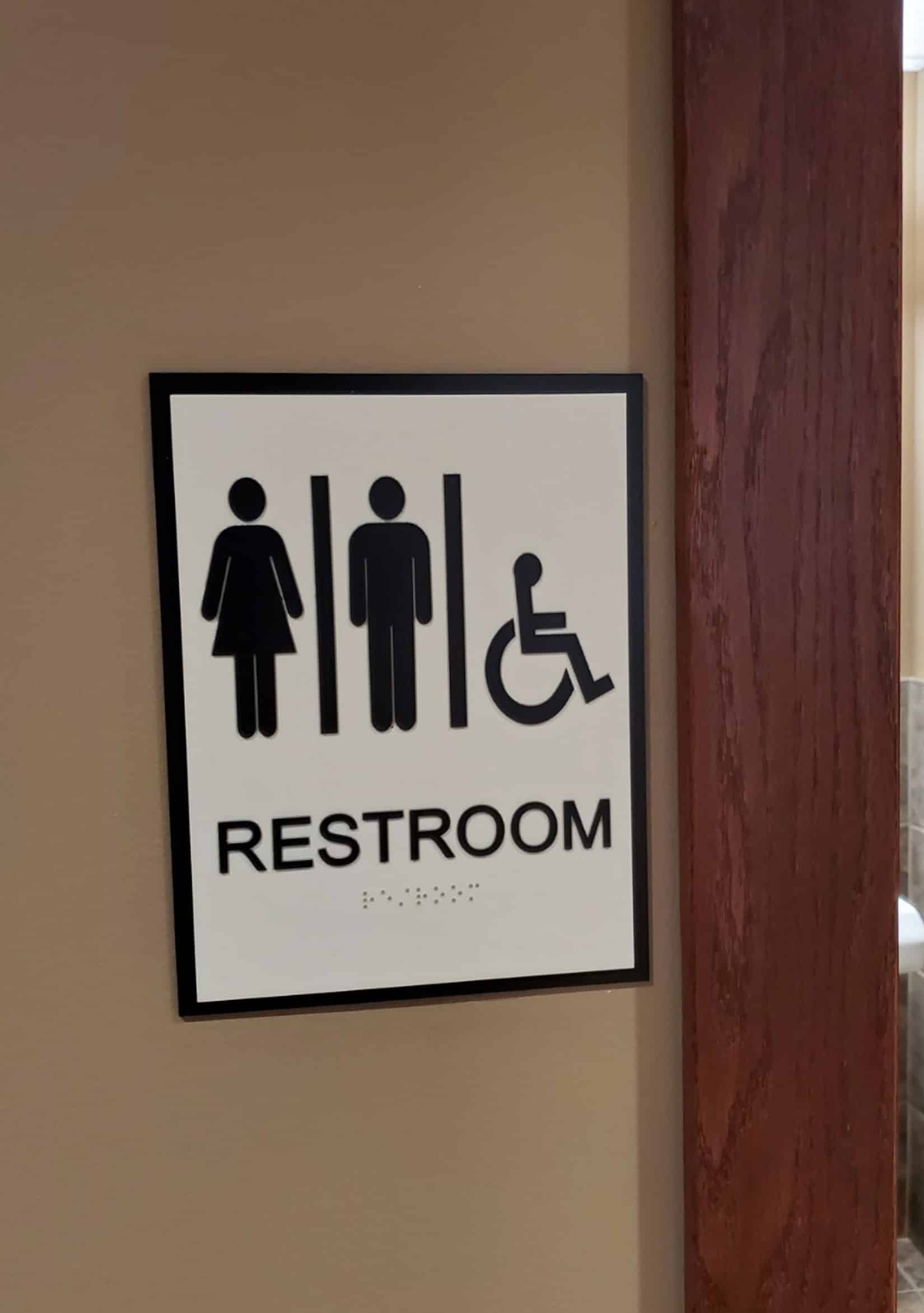 A standard restroom sign hanging inside an office on a tan wall