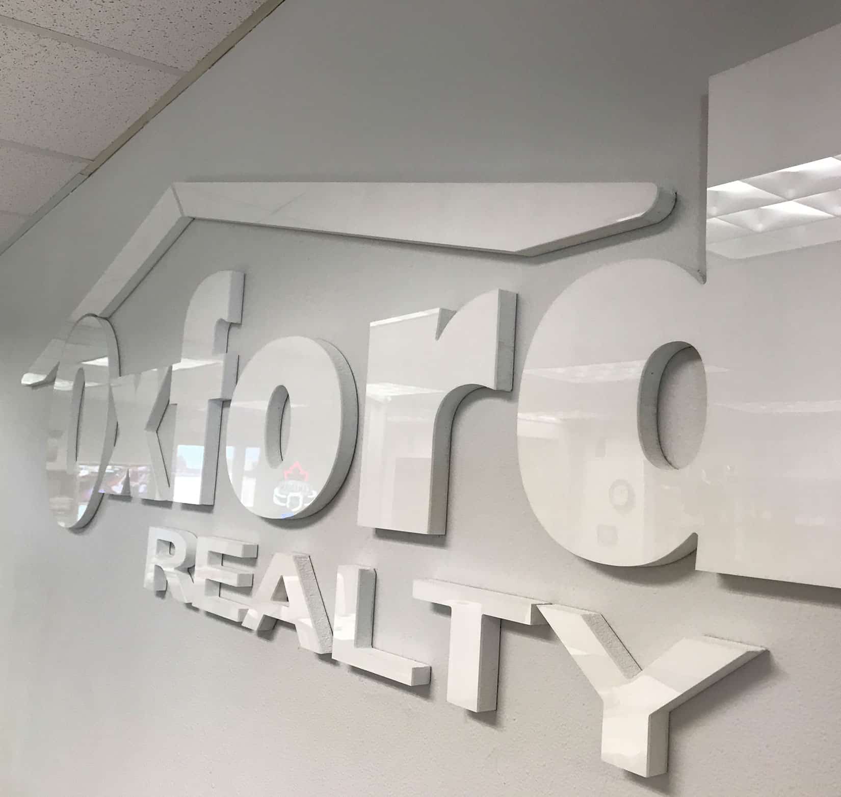 An interior white sign of Oxford Realty’s logo on a white wall