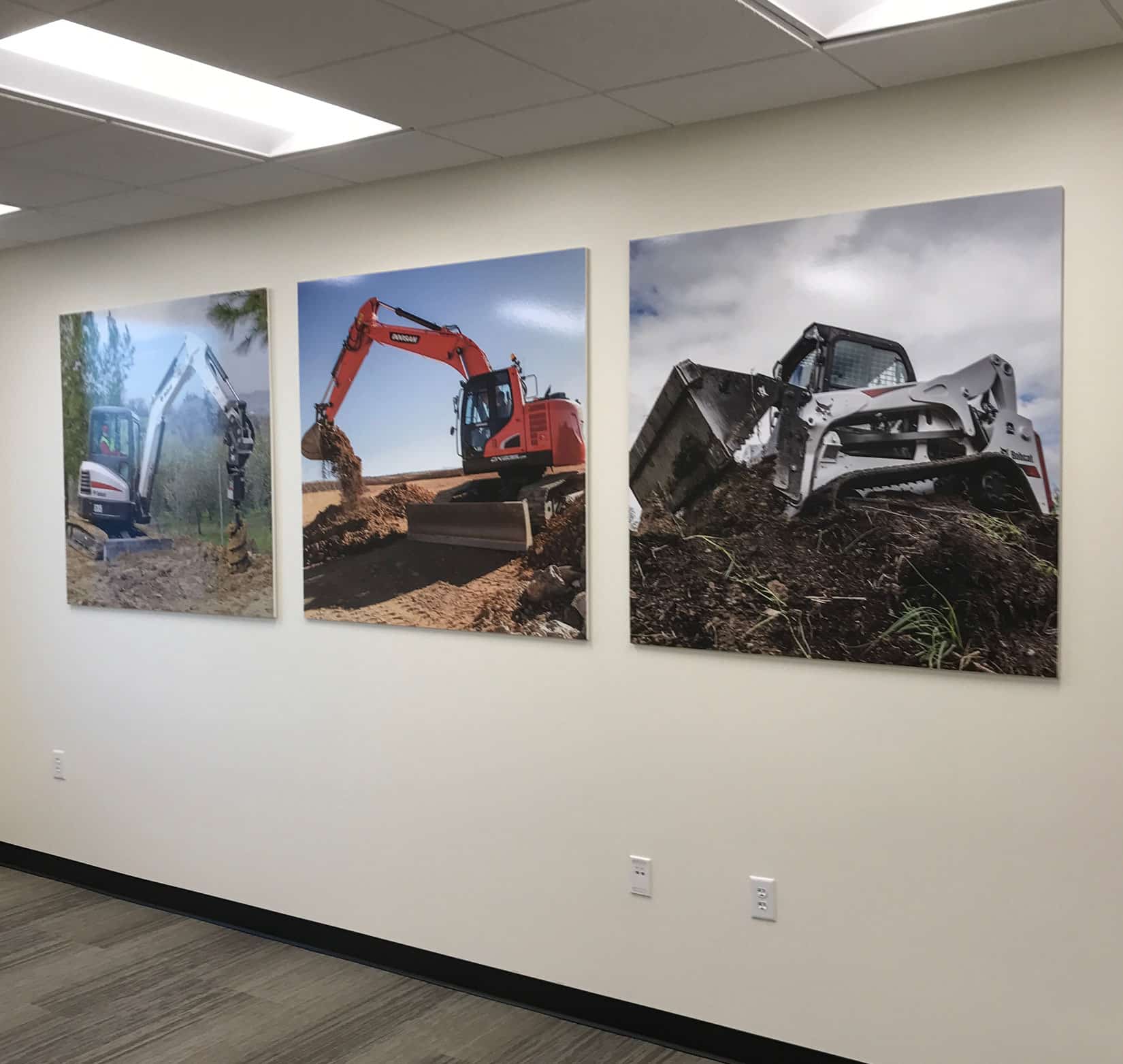 Three interior signs displaying photos of Bobcat machinery on a white wall