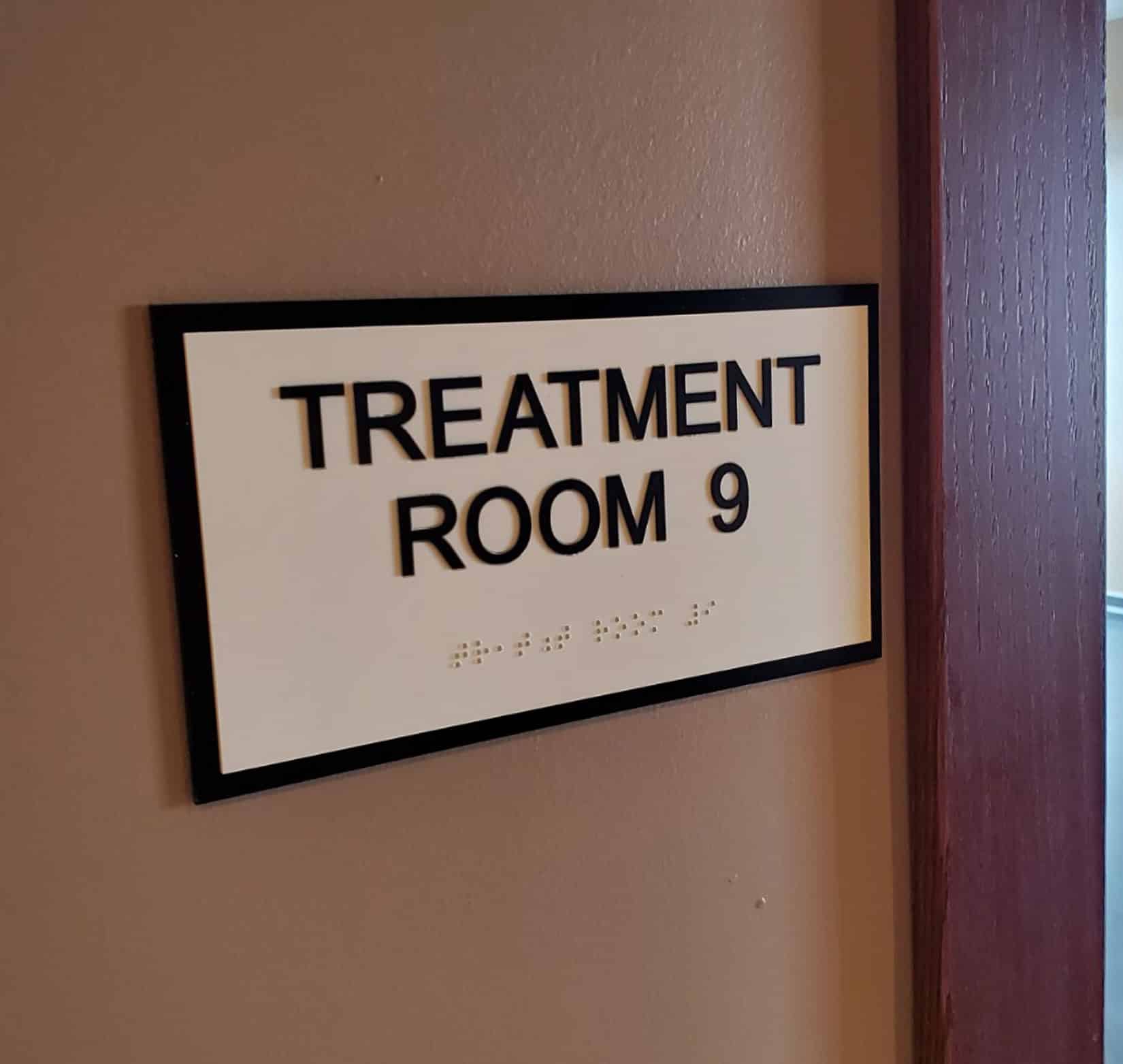 A wall sign that says “Treatment Room 9” in all caps black text on a white background.
