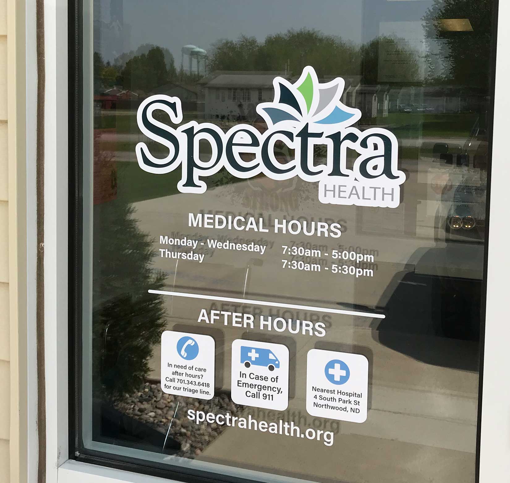 An exterior window sign for Spectra Health with its logo, hours, and website information