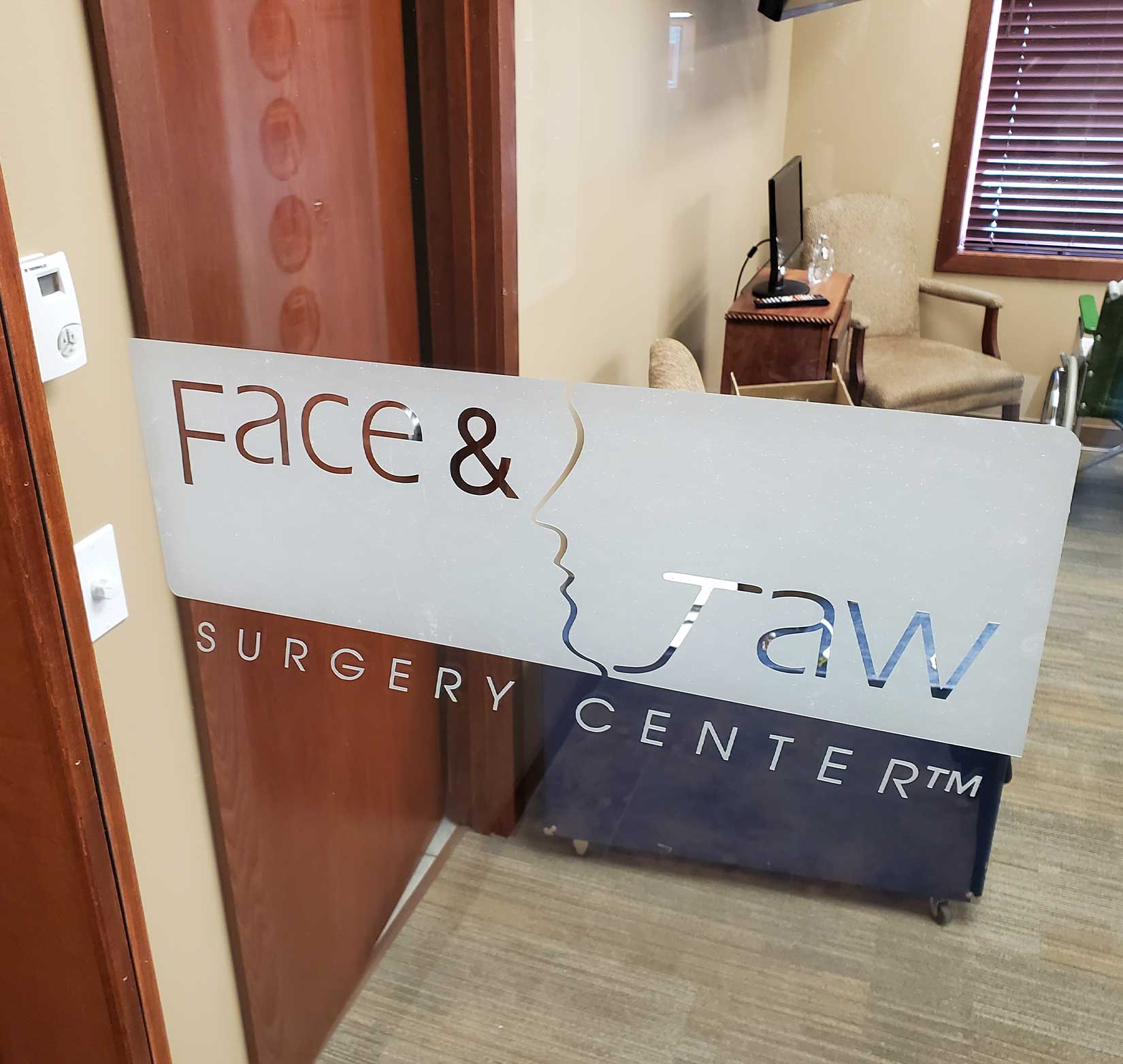 An interior window sign of the Face and Jaw Surgery Center’s logo