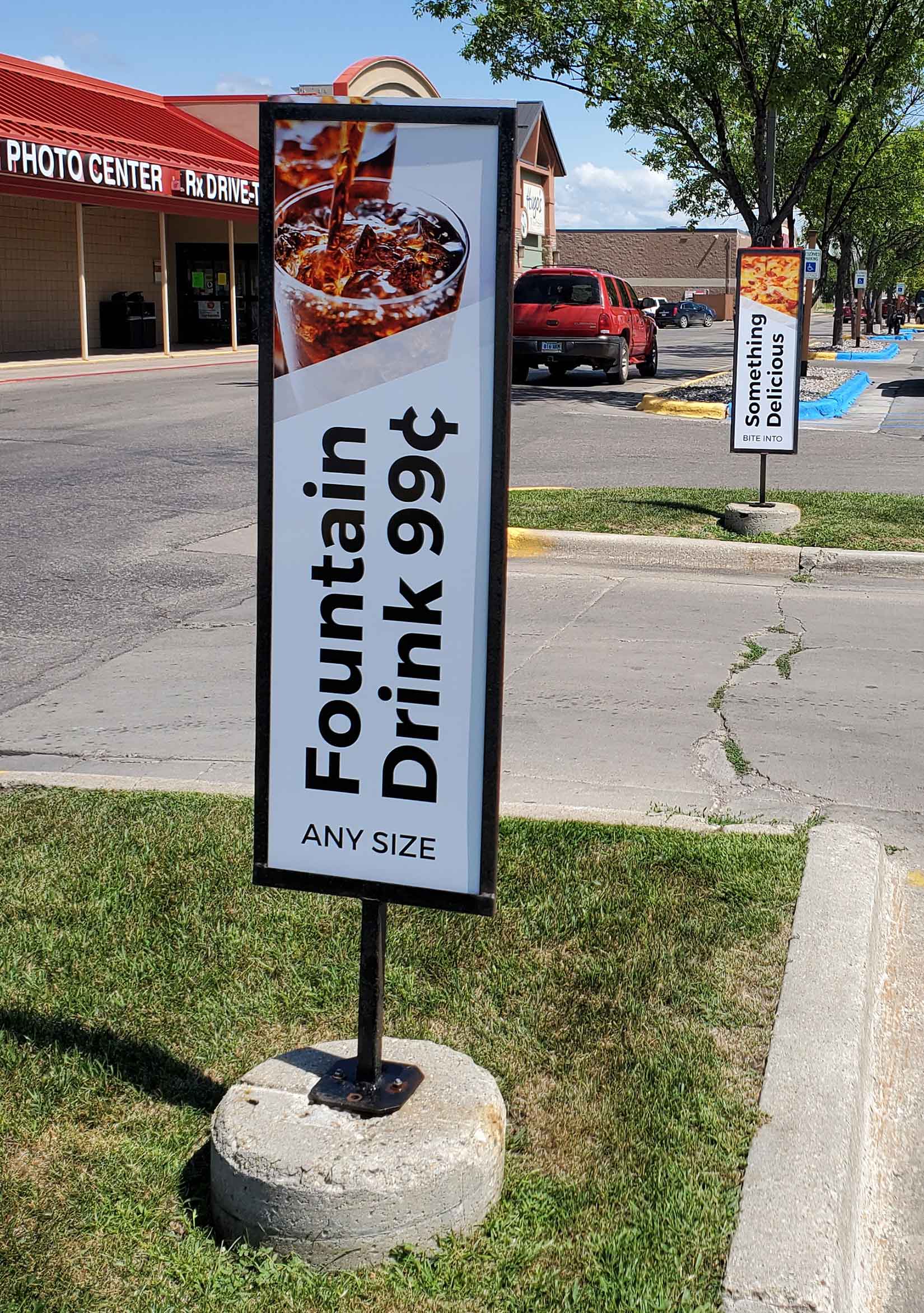 Exterior signage at the entrance to Dusterhoft Family Stores’ parking lot that promote the convenient store’s fountain drinks and food.