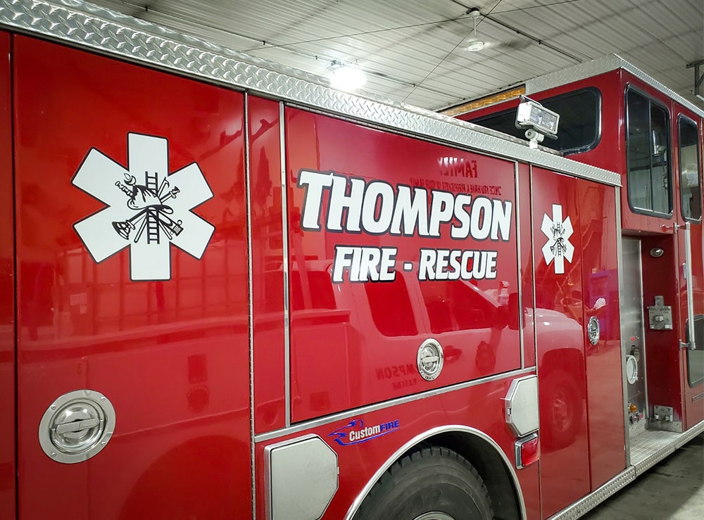 Vinyl lettering that says “Thompson Fire Rescue” in white text on a red firetruck