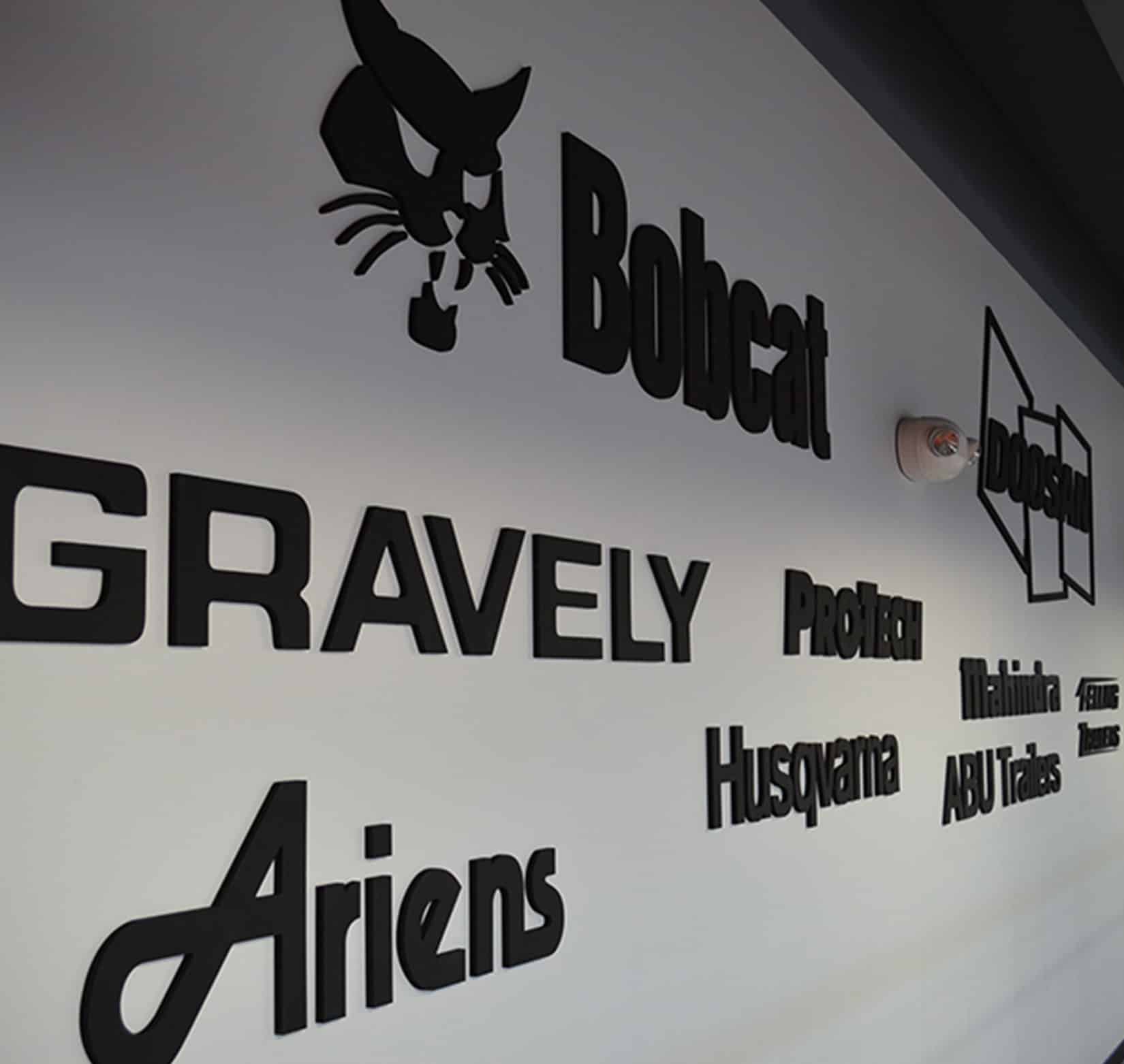 An assortment of black vinyl company logos installed inside Bobcat on a white wall