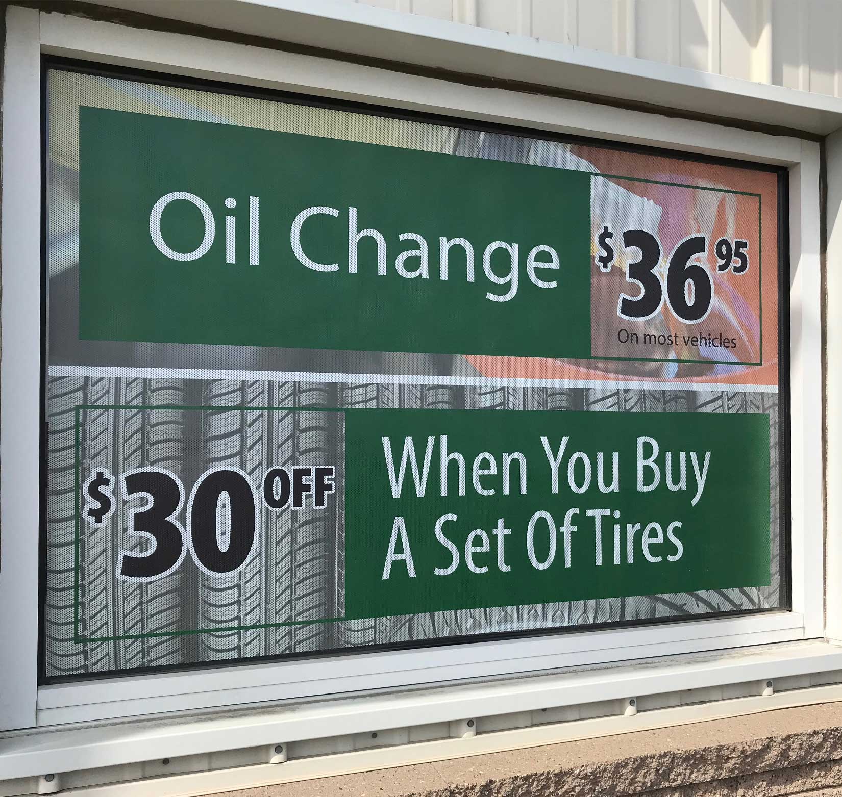 A perforated vinyl window sign displaying the price for an oil change and a discount on tires at Dusterhoft Family Stores.