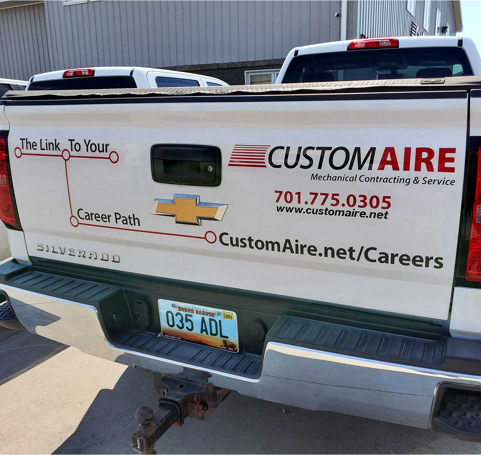 A vinyl wrap on the tailgate of a white fleet truck for Custom Aire.